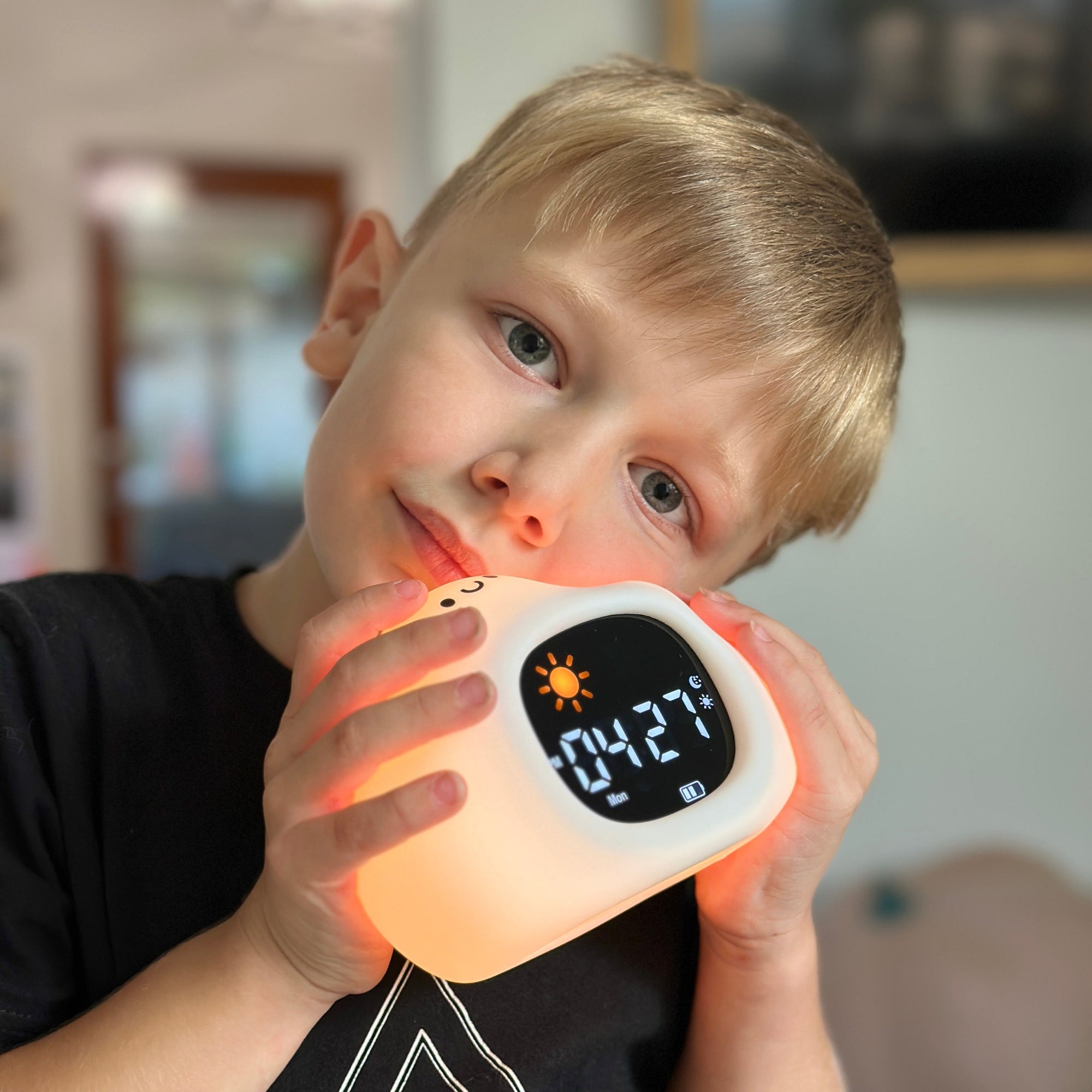 Child holding a digital clock with a glowing face in a home setting