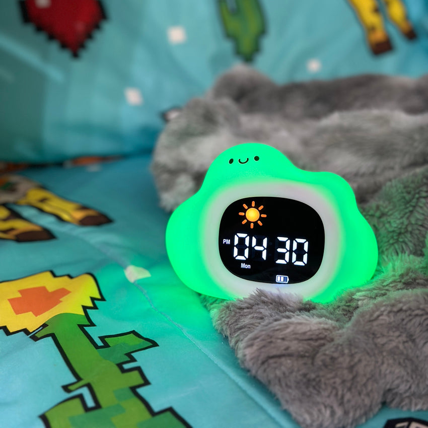Digital clock with green glow on a child's bed with cartoon patterns